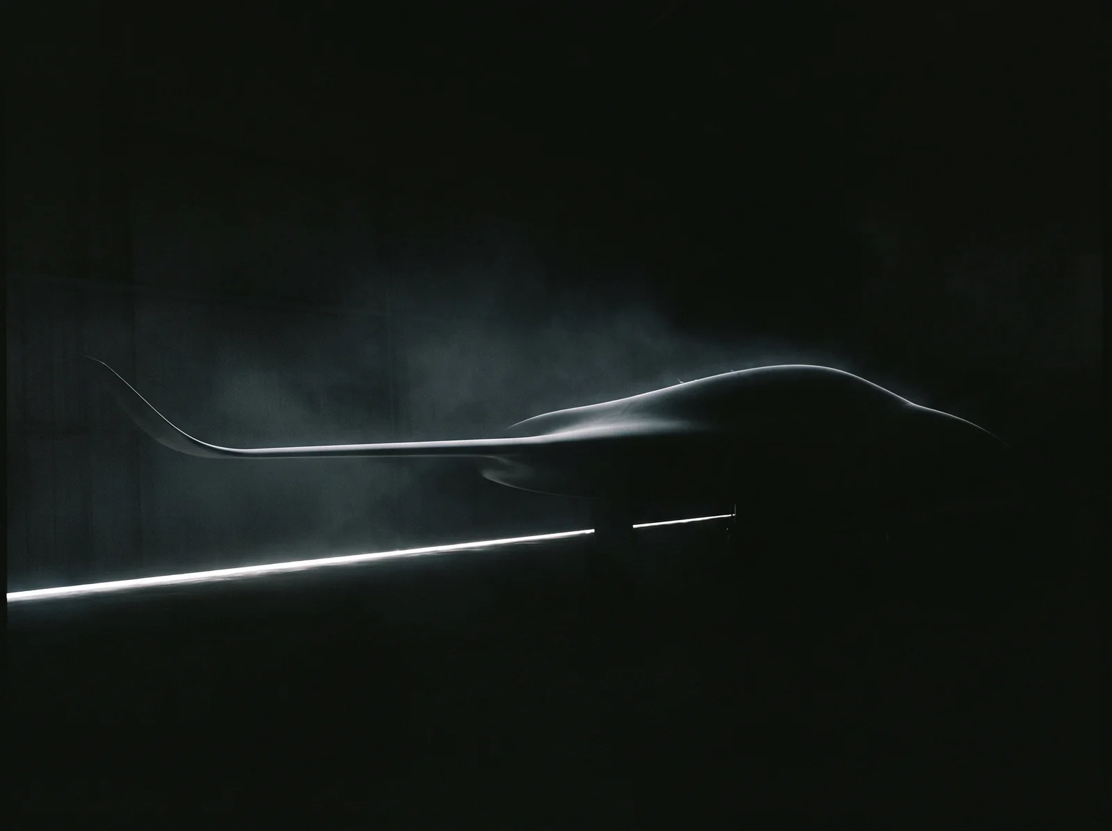 Una aeronave nueva en un hangar oscuro; solo la curva del fuselaje y el ala reciben una delgada línea de luz.